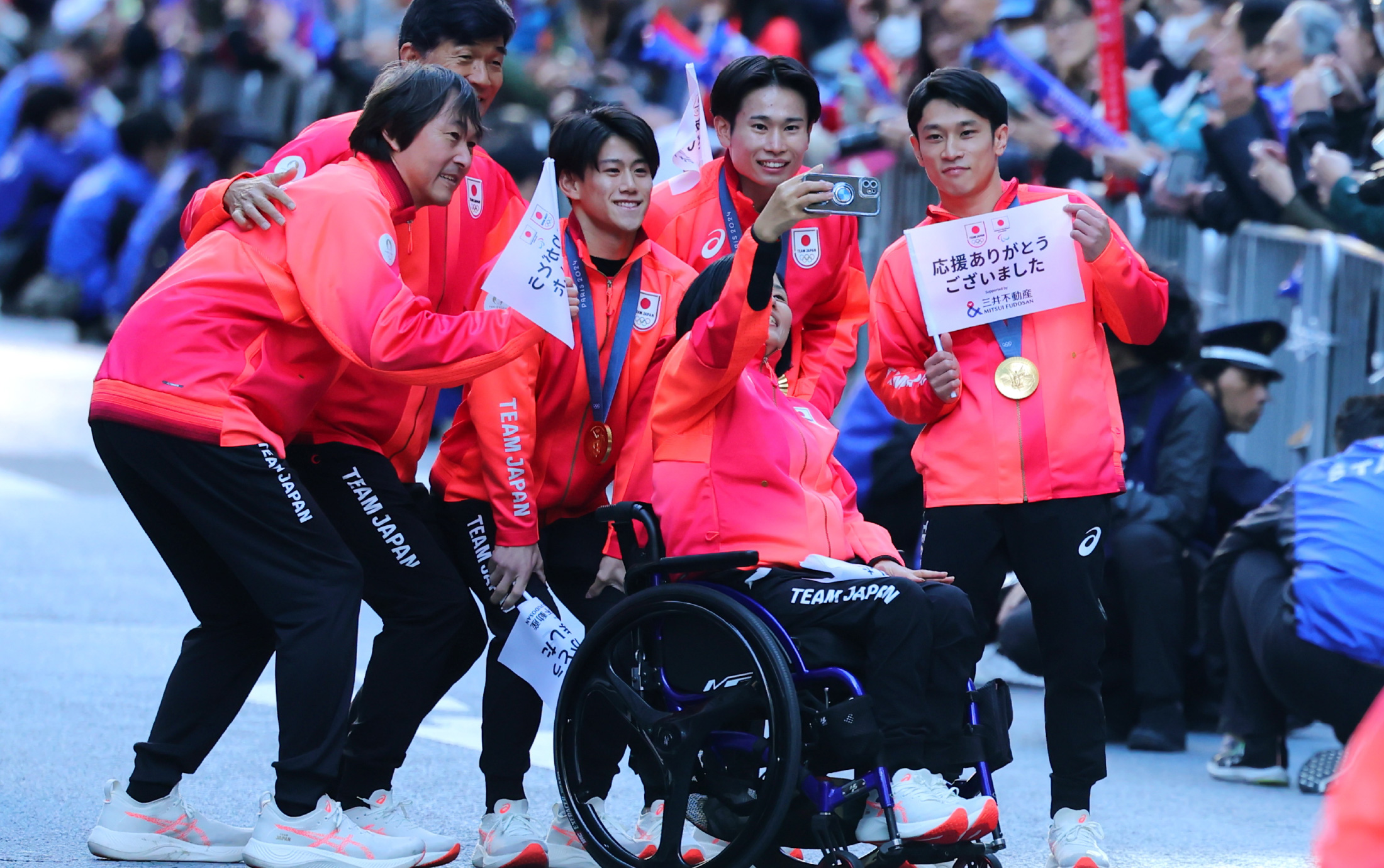 写真：パレードのワンシーン。日本選手一行が笑顔でカメラに「応援ありがとうございました」と書かれた旗を広げて見せている