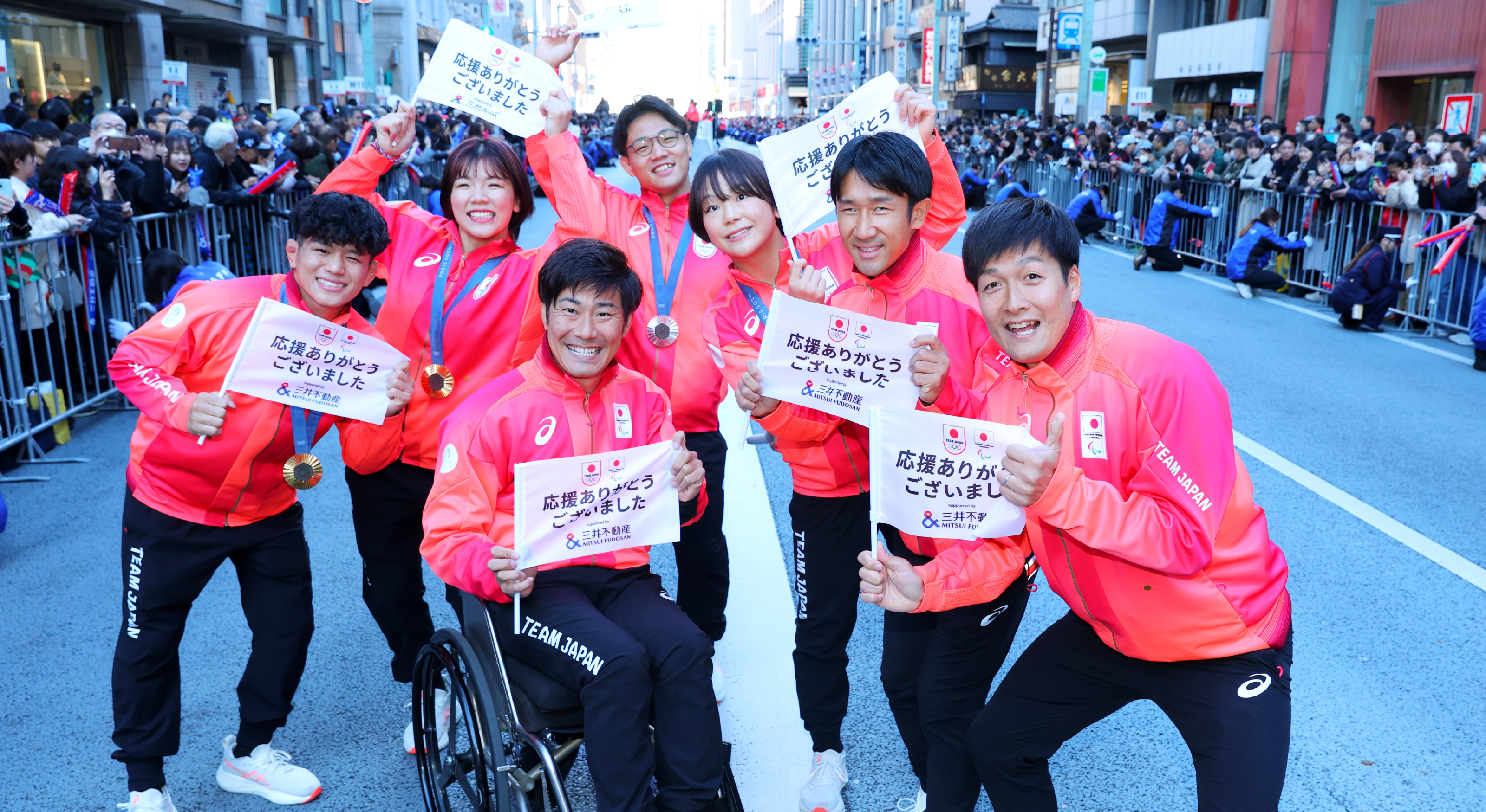 写真：パレードのワンシーン。日本選手一行が笑顔でカメラに「応援ありがとうございました」と書かれた旗を広げて見せている